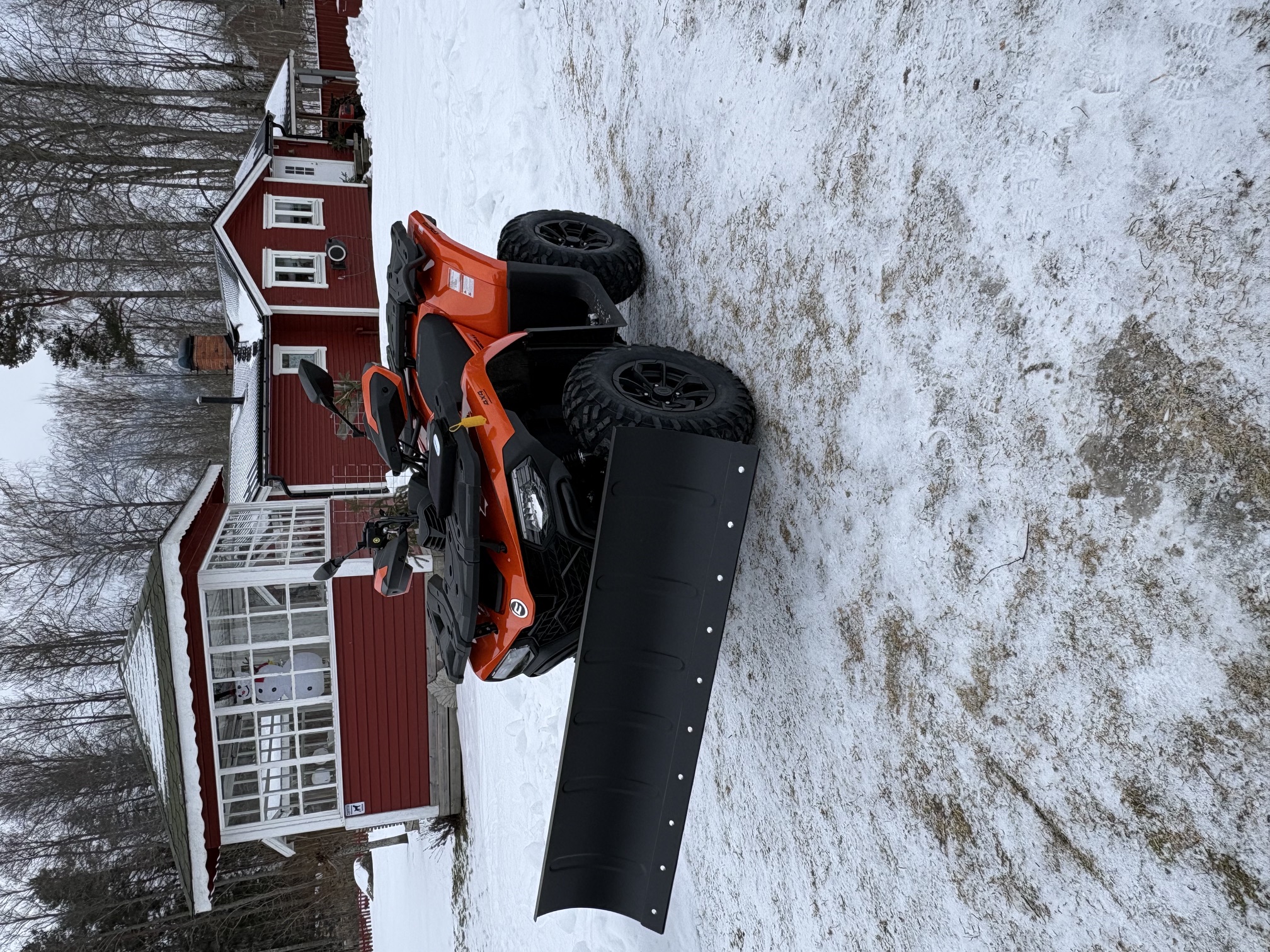 ATV fitted with a snowplow clearing snow at a red house